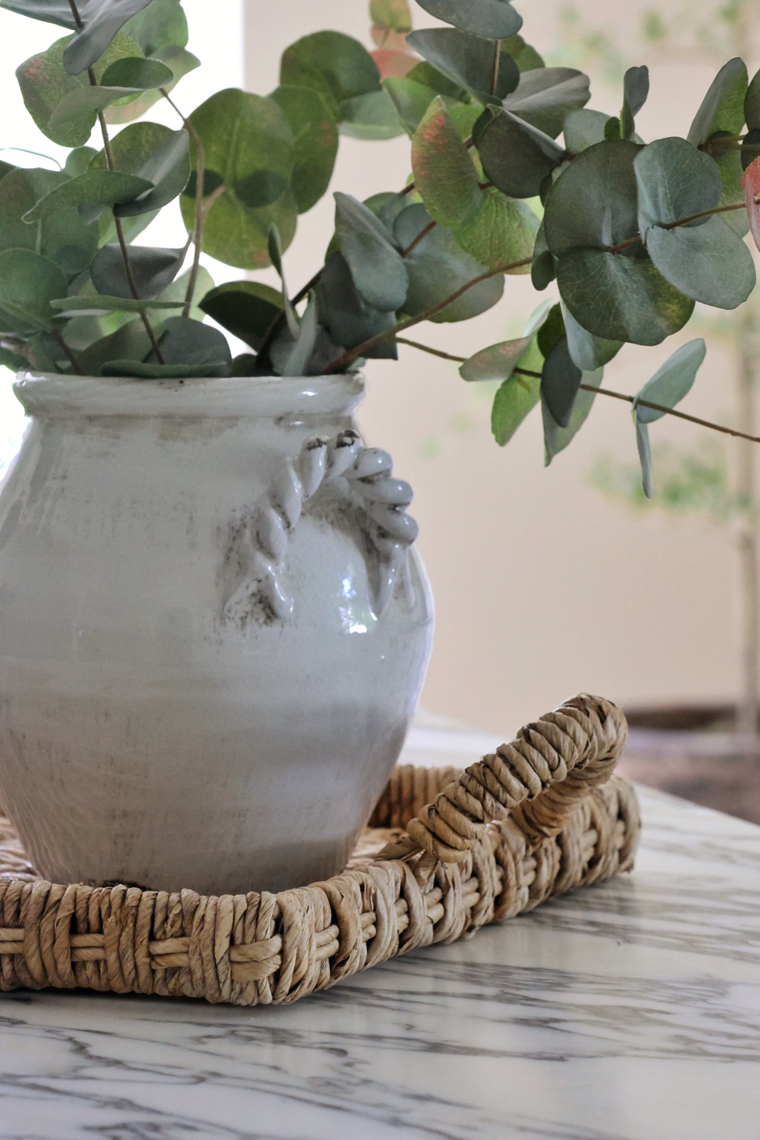 White ceramuc vase with eucalyptus on a woven banana bark tray