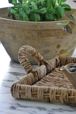 Close up of the handle of a woven banana bark tray with a basil plant behind it 