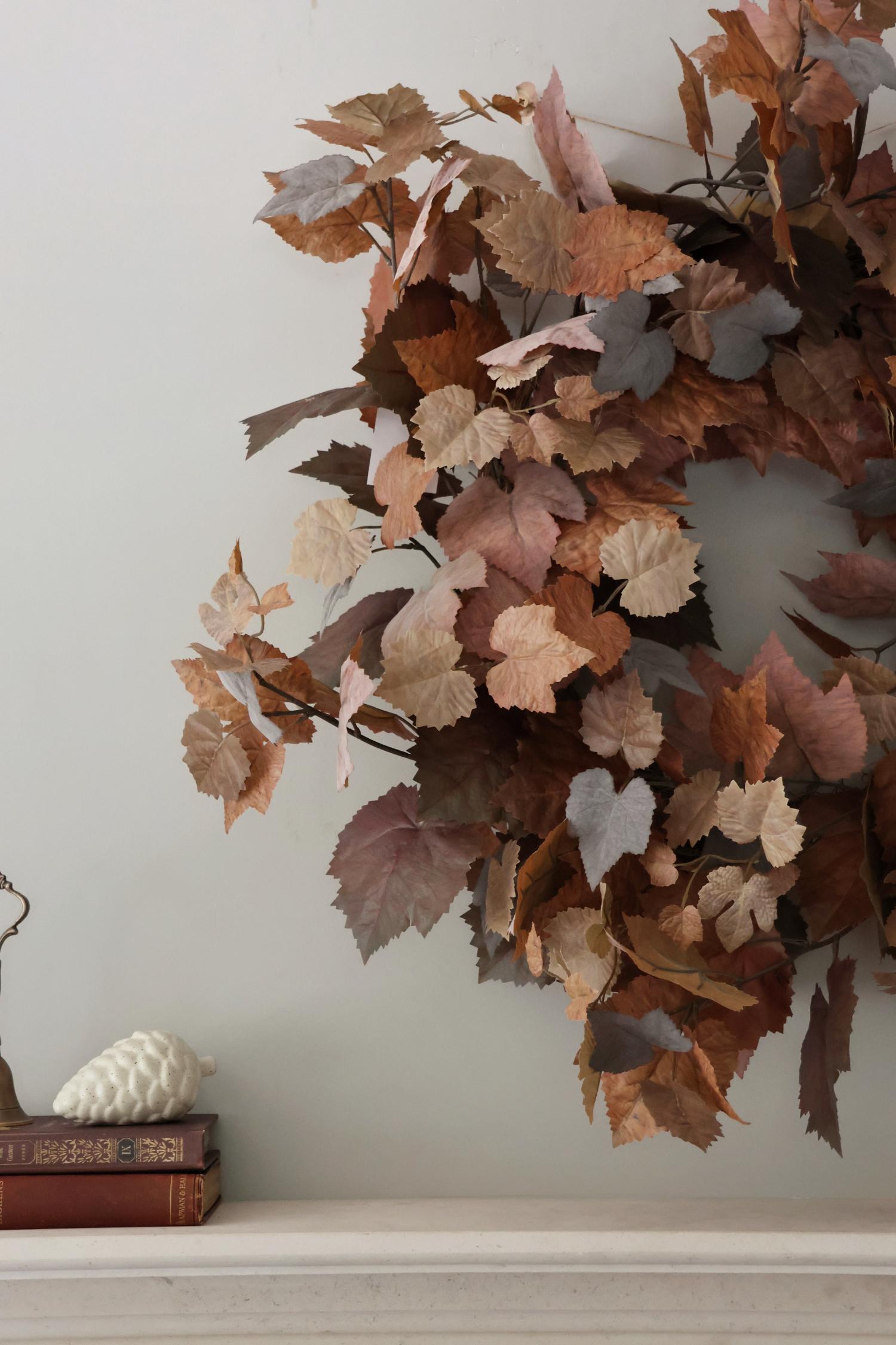 Decorative faux autumn wreath on a white wall with books and a decorative ball below.