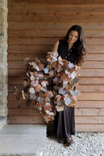 Woman holding a large autumn faux wreath against a wooden wall.