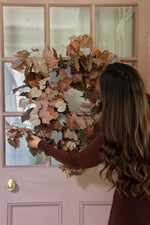 Person adjusting an artificial faux autumn wreath on a door