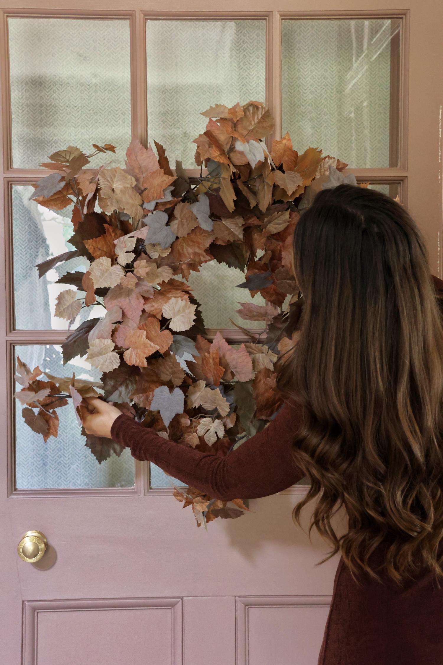 Person adjusting an artificial faux autumn wreath on a door