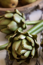 Close-up of artificial green artichokes on a marble surface with a wooden bowl blurred in the background.