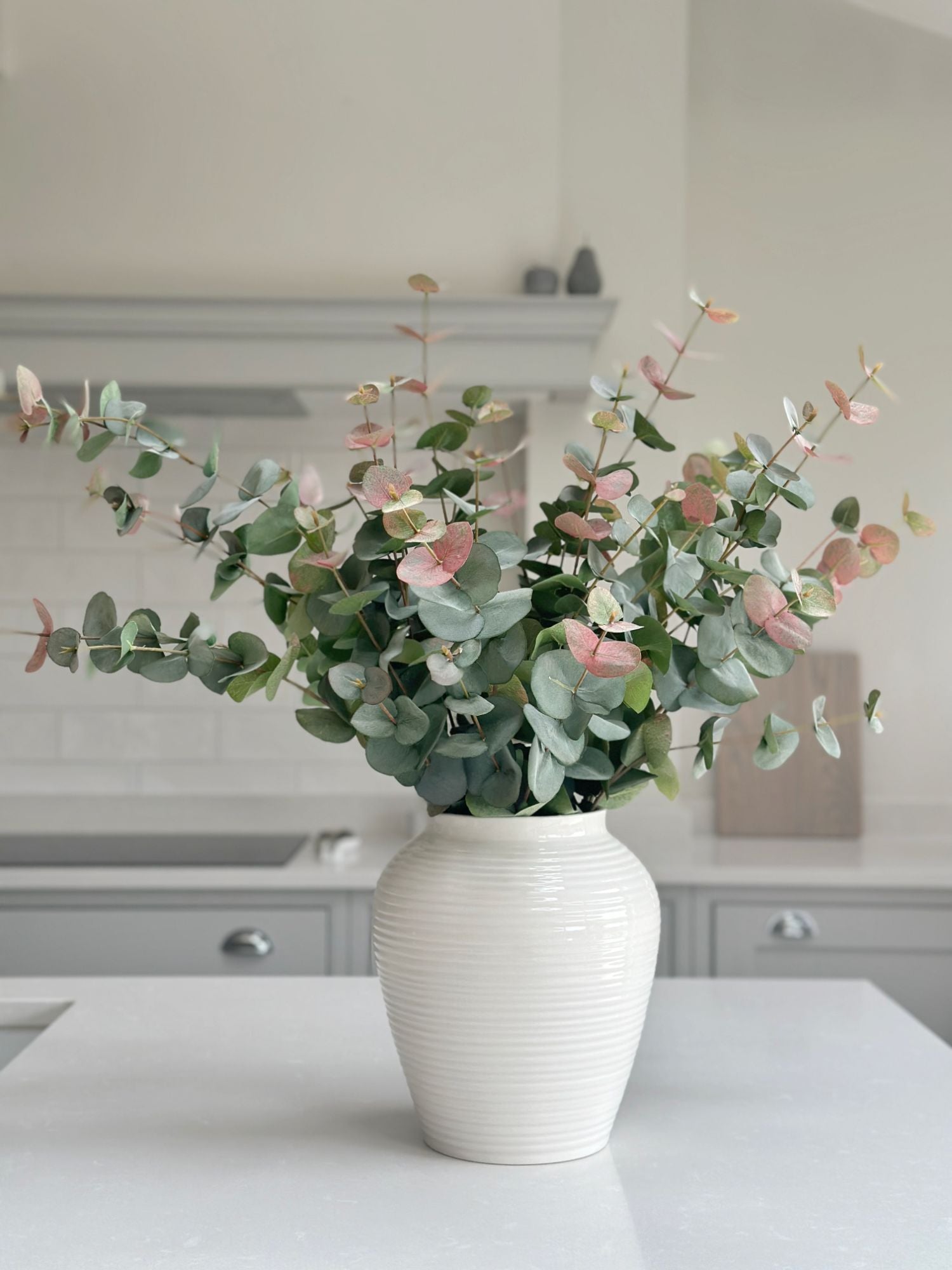 artificial pink tipped eucalyptus in white vase on kitchen island 