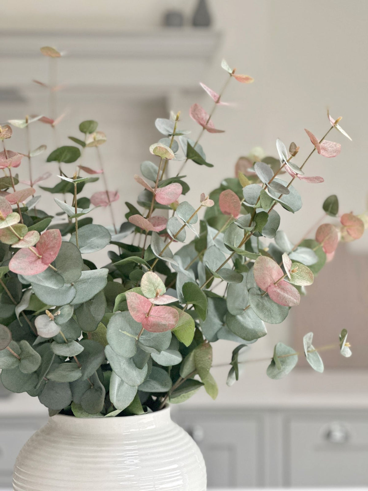 pink tipped eucalyptus stems in white vase