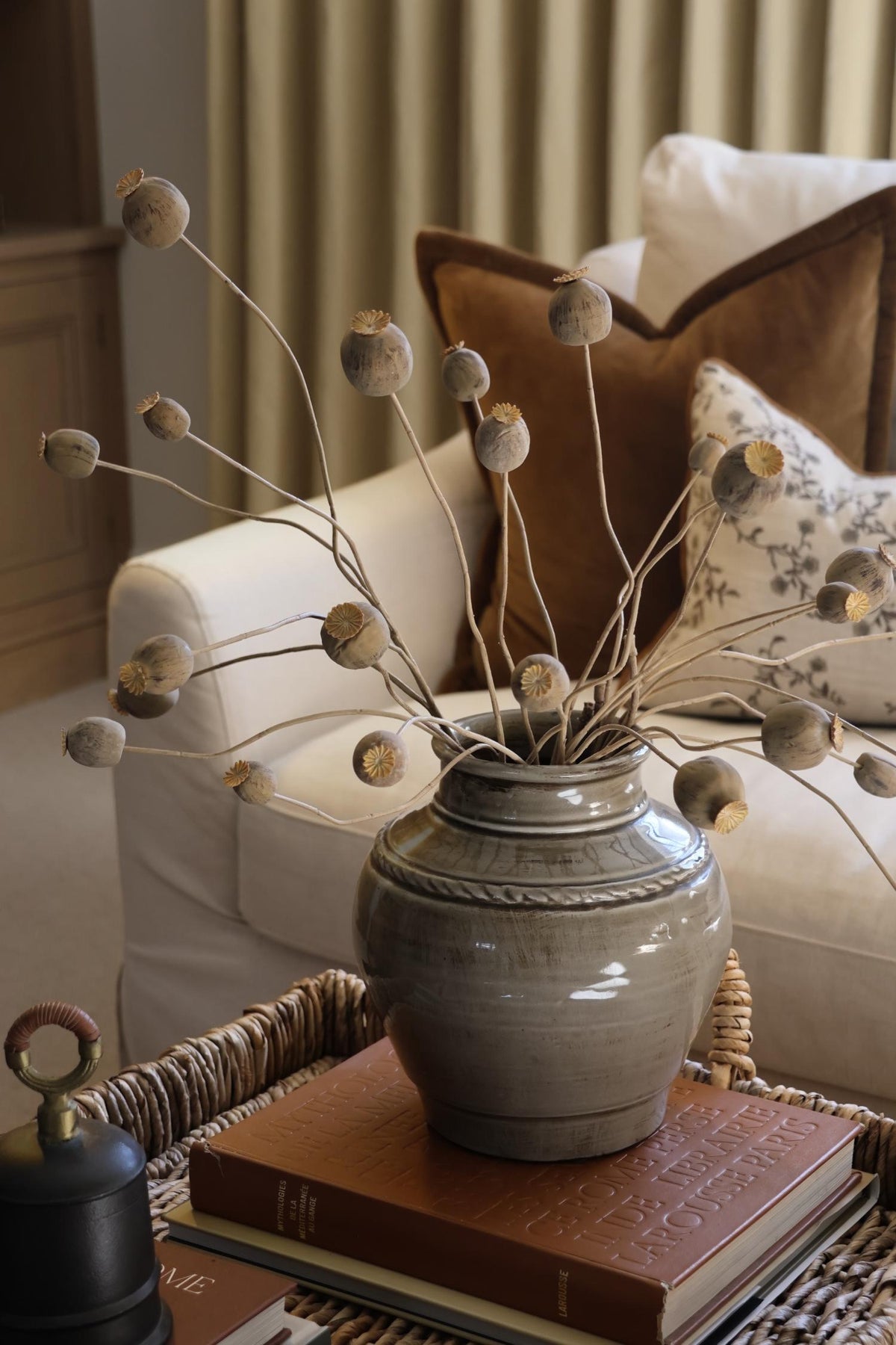 artificial dried poppy spray styled in a grey ceramic vase on a coffee table