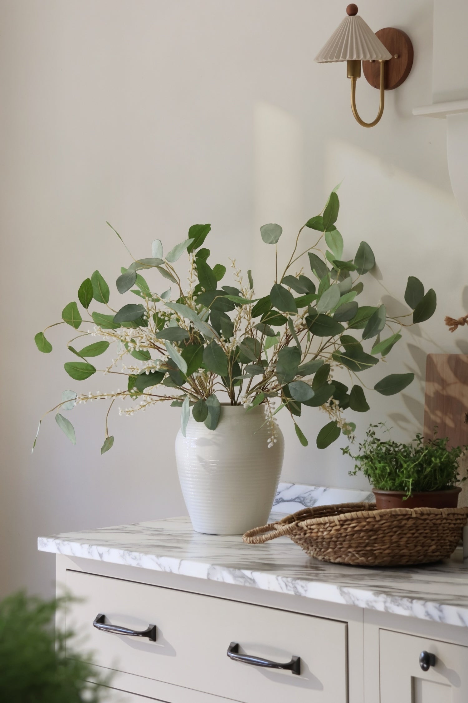 White vase with artificial eucalyptus on a marble countertop with a neutral background