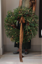 women holding a large faux green wreath with dark brown velvet ribbon