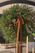 large artificial larix wreath with lots of scattered pinecones and brown velvet ribbon