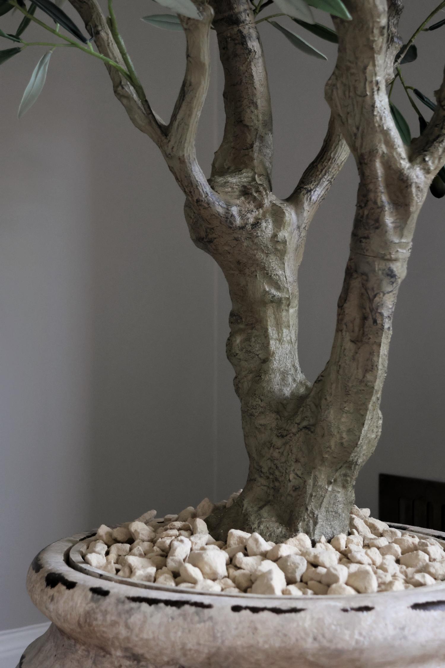 close up of a faux olive tree brown trunk with pebbels ontop of the planter 