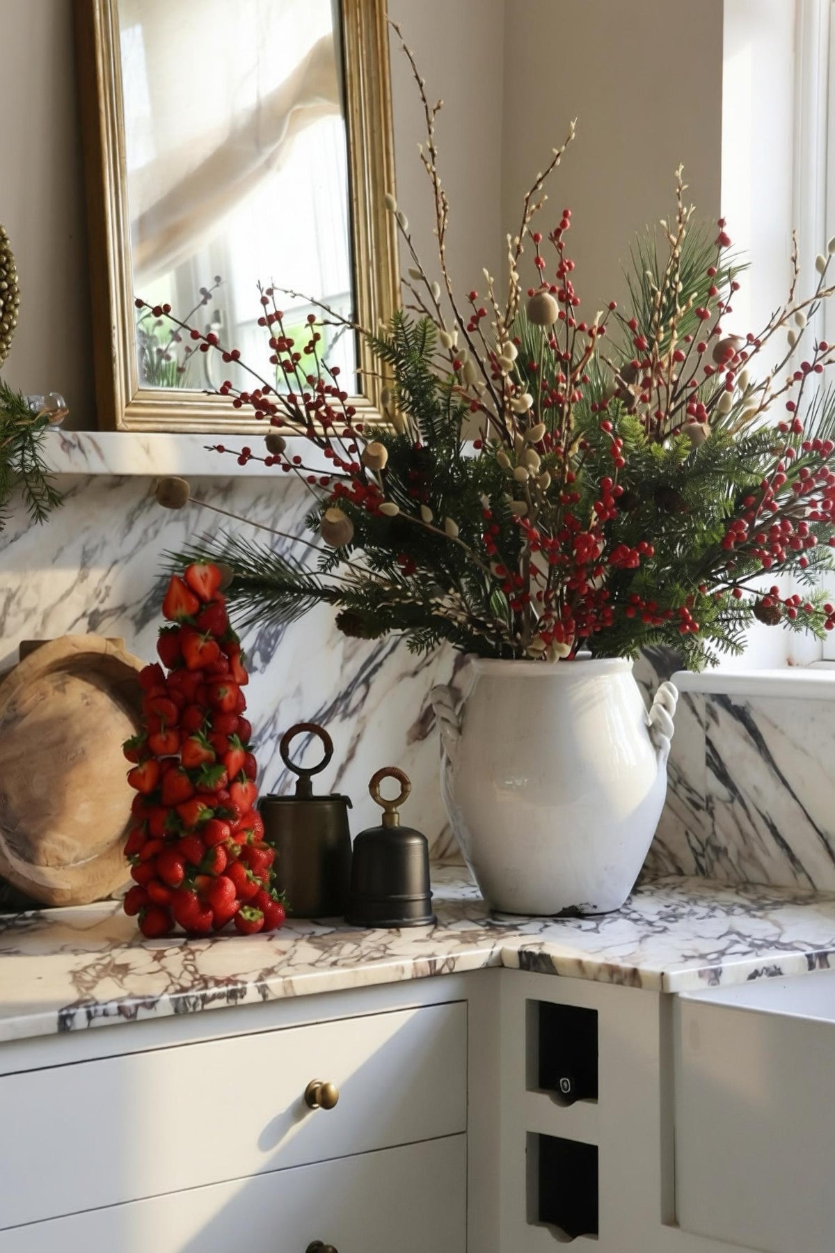 artificial red berry festive arrangement in large white ceramic vase on marble kitchen worktop 