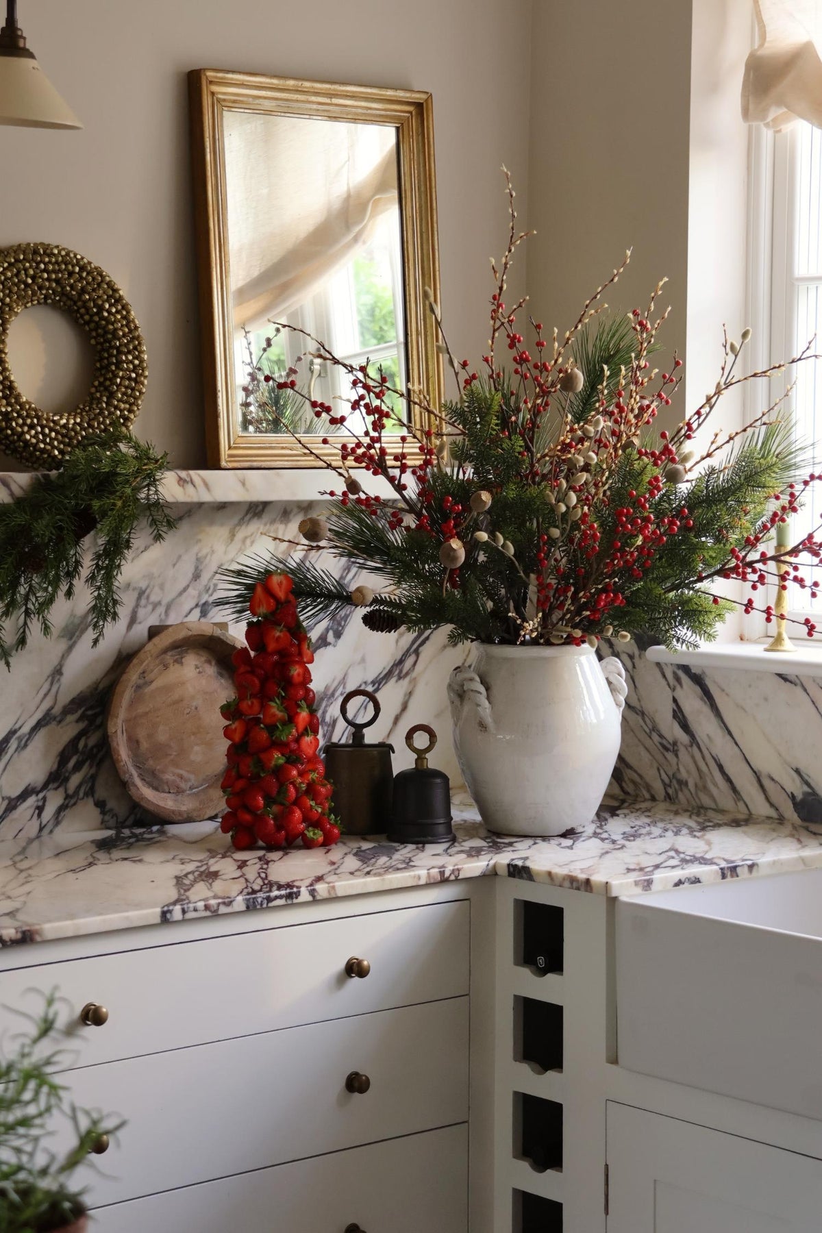 artificial red berry festive arrangement in large white ceramic vase in marble kitchen scene