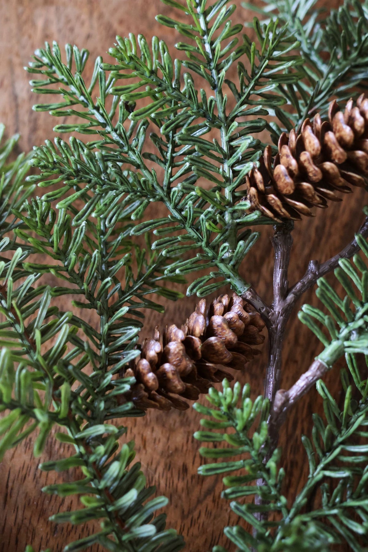 close up photo of a faux spruce branch with green foliage and brown pinecones 