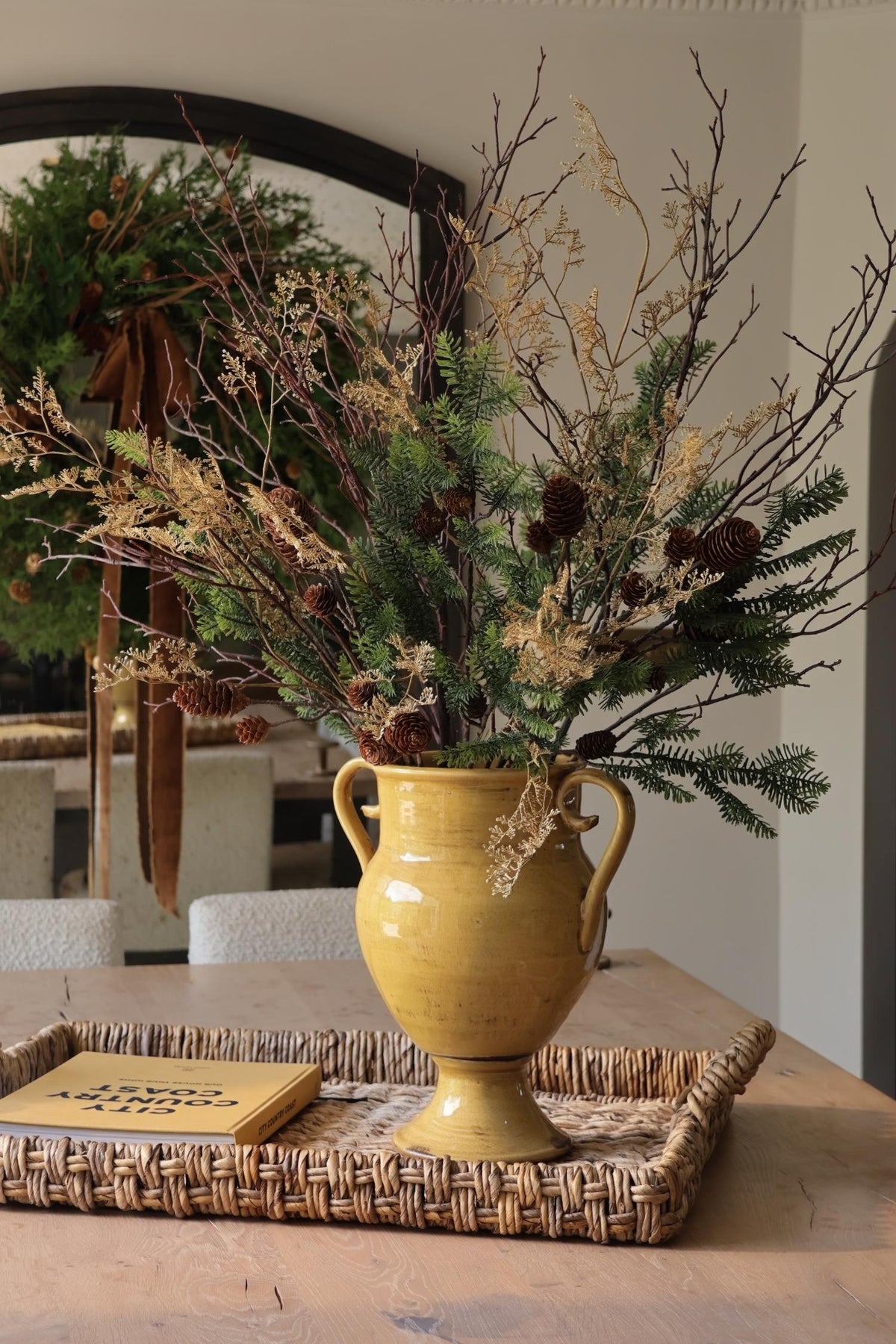 artificial winter foliage arrangement in yellow vase on rattan tray 