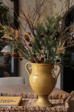 artificial winter foliage arrangement in yellow vase on rattan tray 
