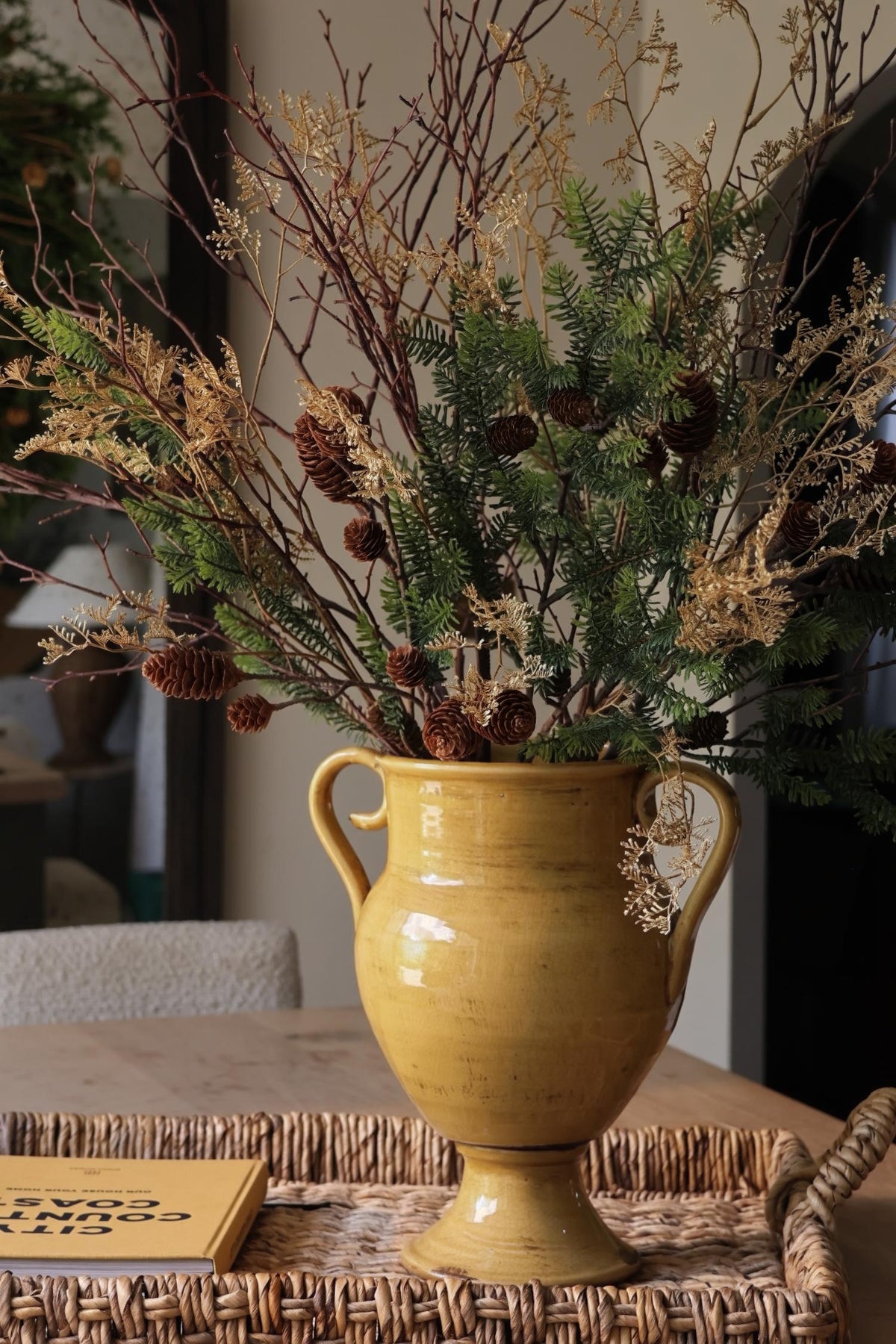 artificial winter foliage arrangement in yellow vase on rattan tray 