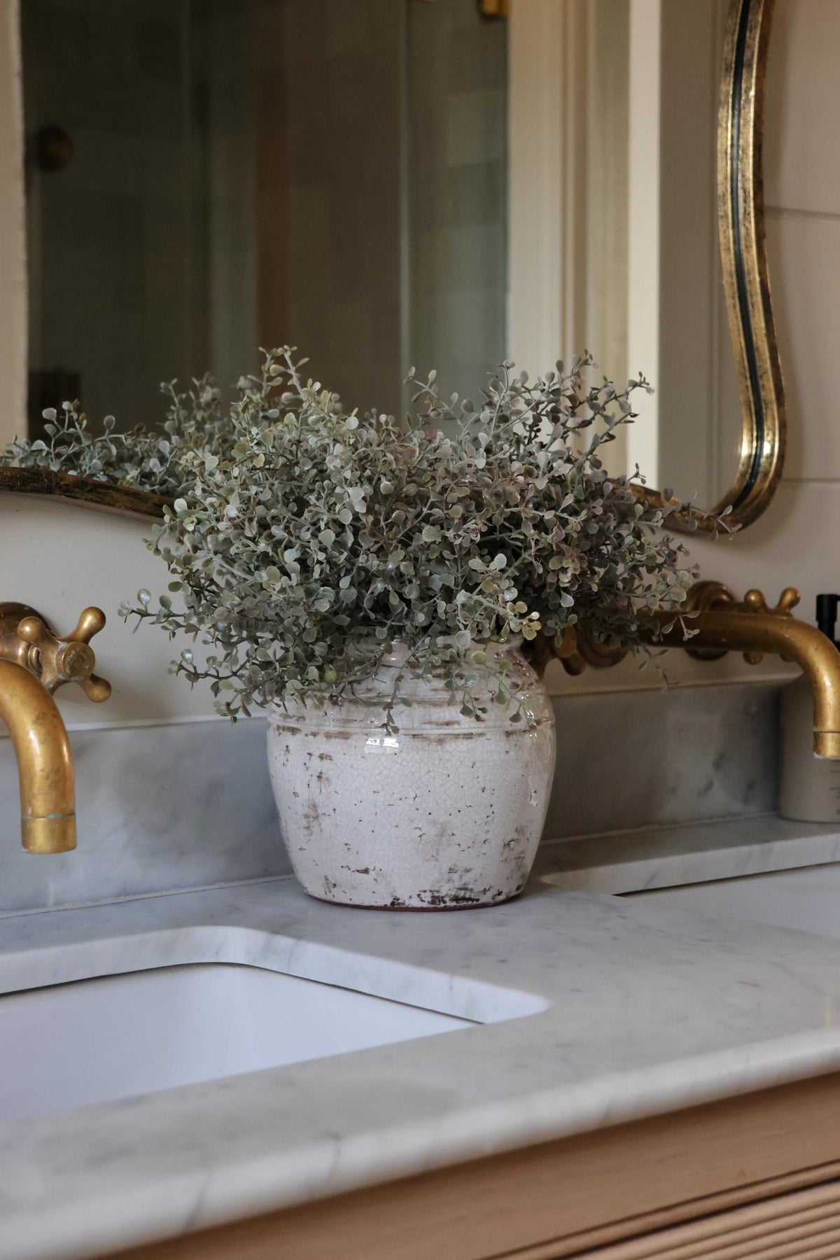 bentley pot and eucalyptus faux bush on a marble sink surface of a double vnanity bathroom unit 