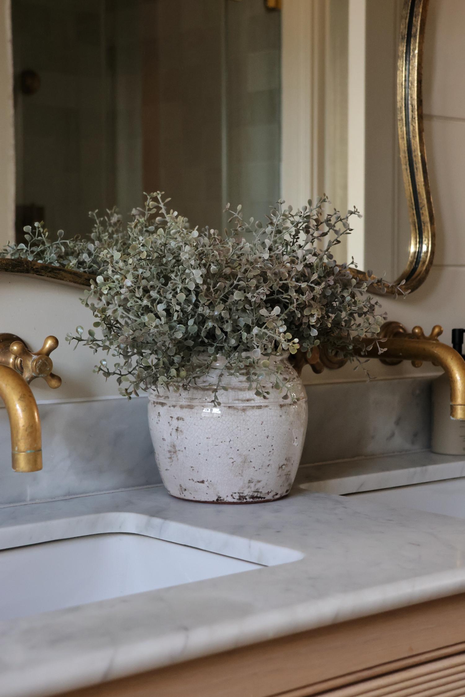 bentley pot and eucalyptus faux bush on a marble sink surface of a double vnanity bathroom unit 