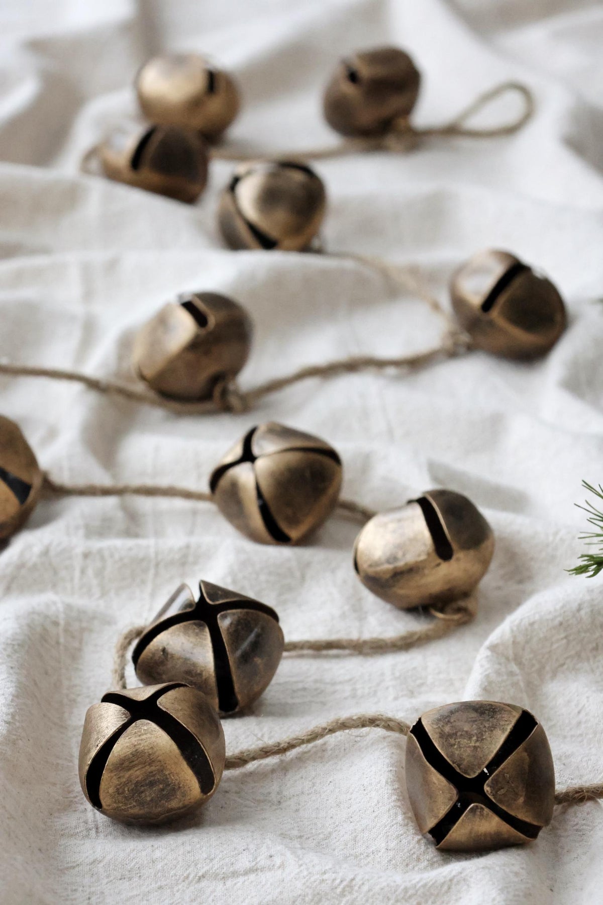 A series of brass jingle bells tied to a natural jute rope, displayed on a white fabric surface.