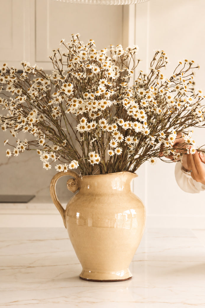 Beige ceramic jug with white daisy flowers on a light wooden surface