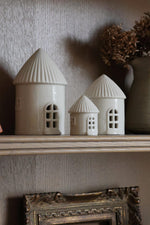 Two small ceramic buildings on a shelf with a textured wall background