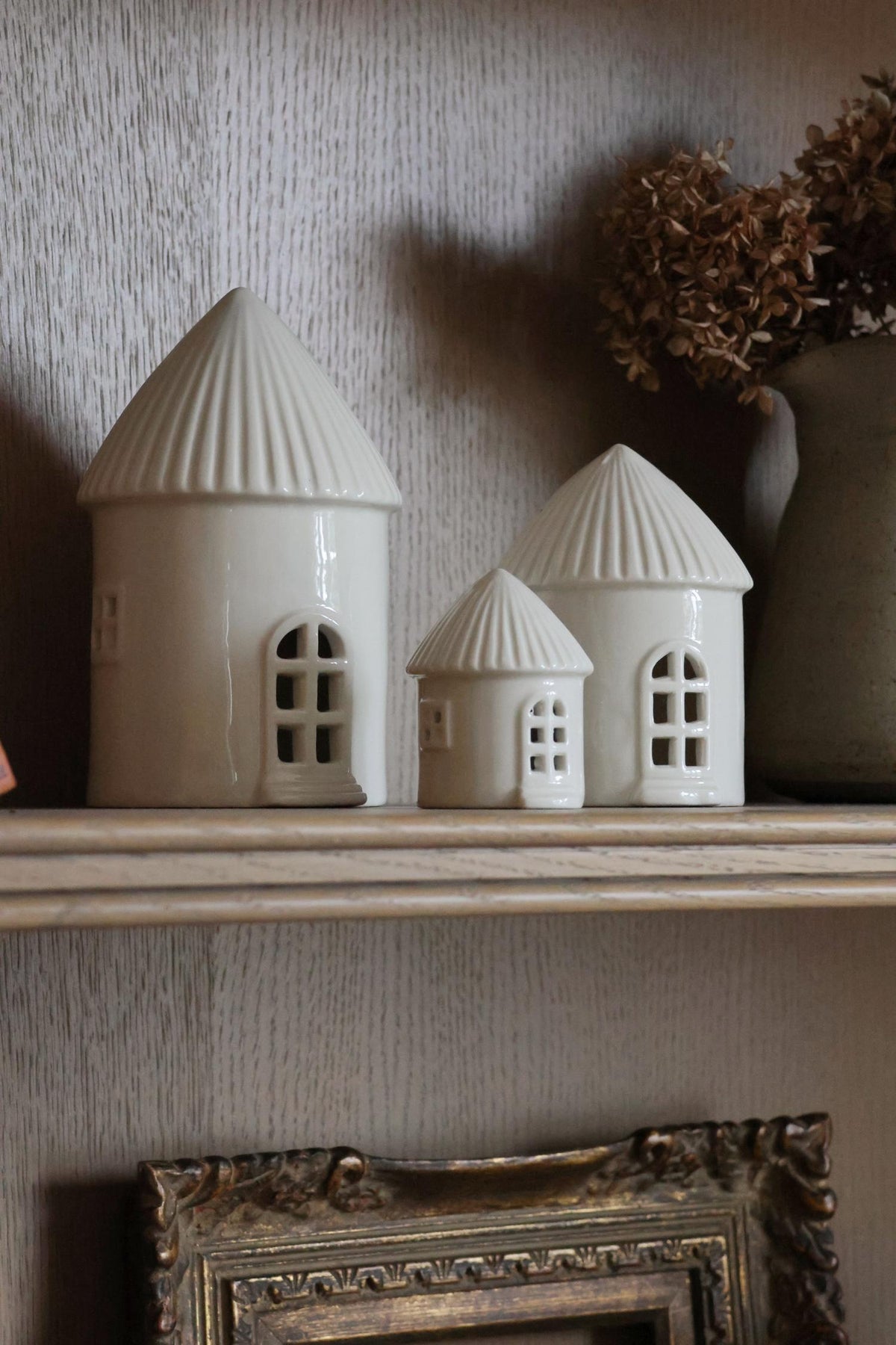 Two small ceramic buildings on a shelf with a textured wall background