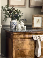 Decorative setting with a wooden cabinet, vase with greenery, small houses, and framed picture.