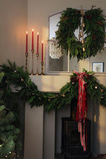 Large artificial xmas wreath and garland with red accent ribbon and candles in a cosy living room setting