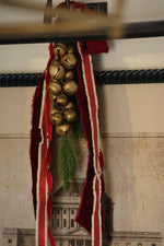 cluster of brass bells and red ribbons hanging from a picture fram 