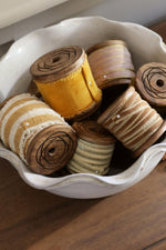 velvet ribbons on wooden spools in a pie crust edge ceramic white bowl on wooden surface