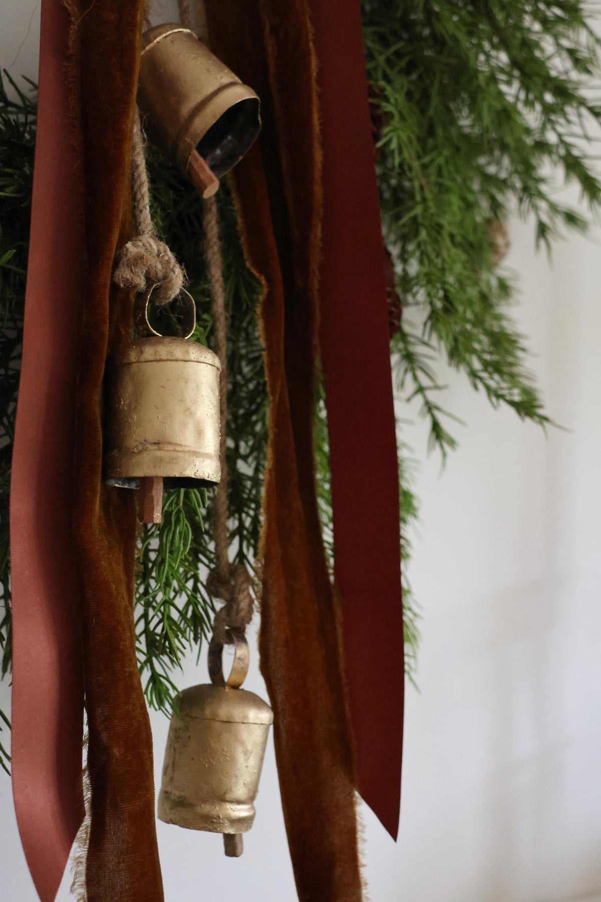 brass cowbells hanging on a wreath with brown ribbon on plain wall 