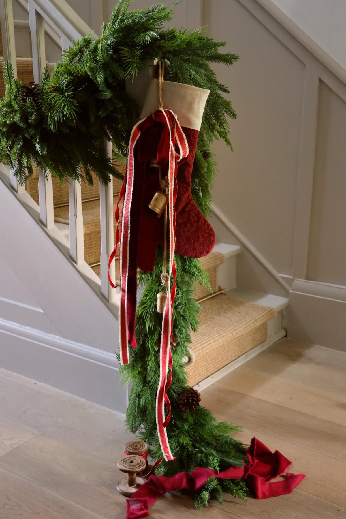 staircase dressed with green artificial foliage garland and red velvet stocking with brass bells and ribbons 
