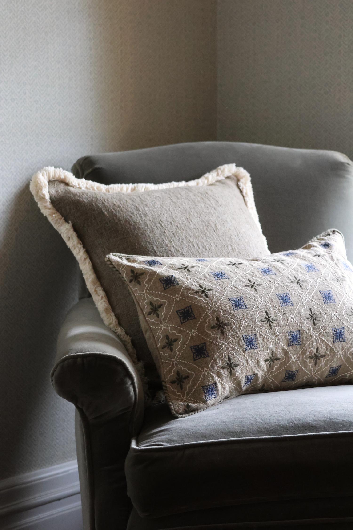 Two patterned cushions on a gray armchair against a neutral wall.