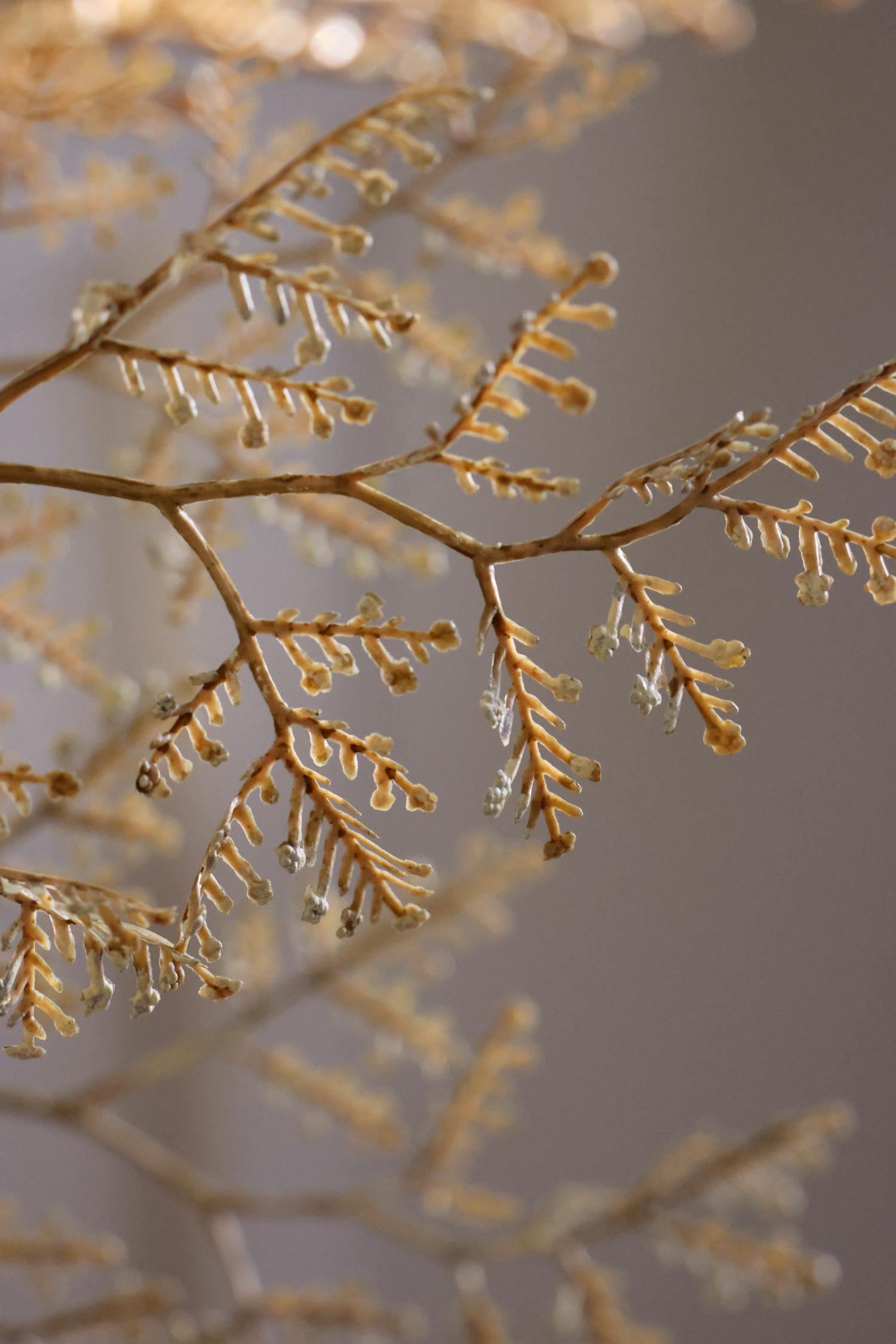 A close-up of delicate golden-brown branch-like decor with small icicles and clear hanging droplets against a soft blurred taupe background.