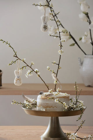 Small cake on a stand with white flowers and decorative elements on a wooden surface.