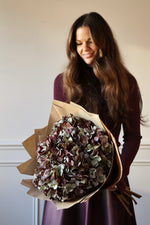 Large bouquet of Faux Mulberry hydrangeas wrapped in brown paper held by women in purple dress 