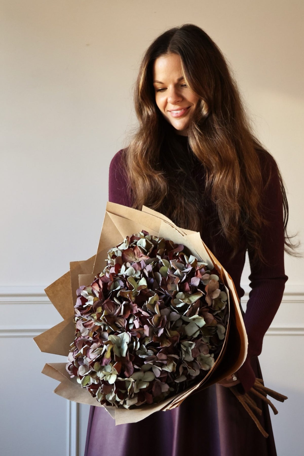 Large bouquet of Faux Mulberry hydrangeas wrapped in brown paper held by women in purple dress 