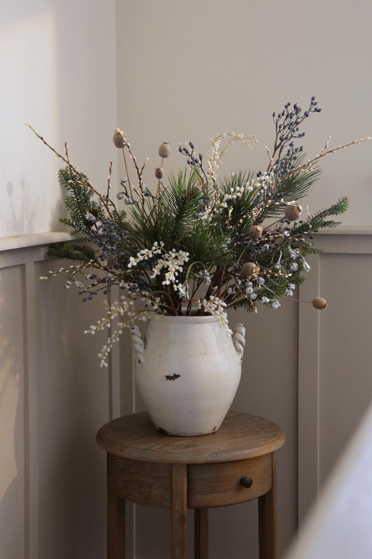 faux blue berry festive arrangement in white vase on wood sidetable 