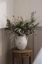 faux blue berry festive arrangement in white vase on wood sidetable 