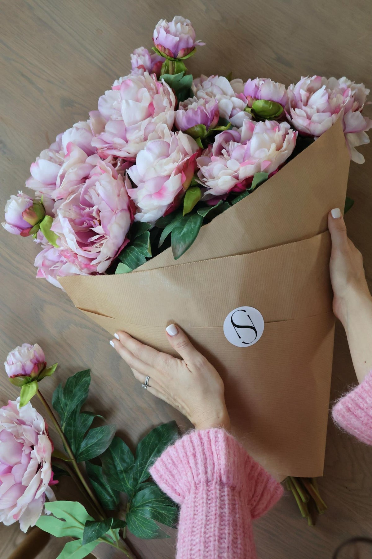faux blush pink peony stems wrapped in brown paper on wooden able