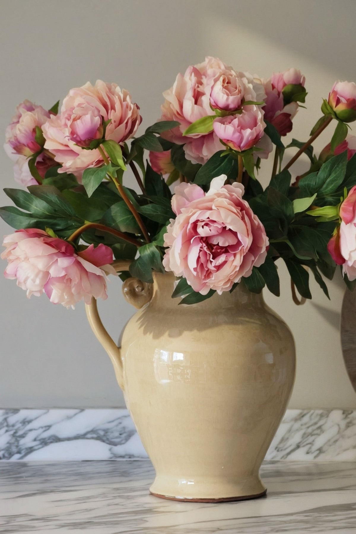 Beige vase with pink flowers on a marble surface