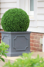 Decorative artificial buxus topiary ball with a spherical green bush in front of a house.
