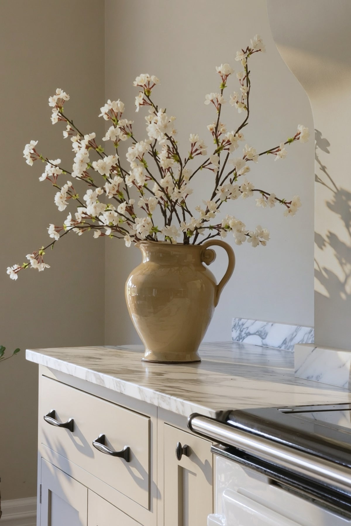 Beige cavendish  ceramic vase with white cherry blossom flowers on a kitchen counter