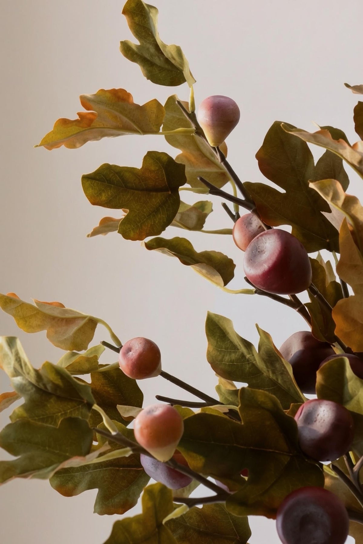 artificial autumn leaves in muted green and orange with fig in deep plum and burgundy tones on a blurred background 