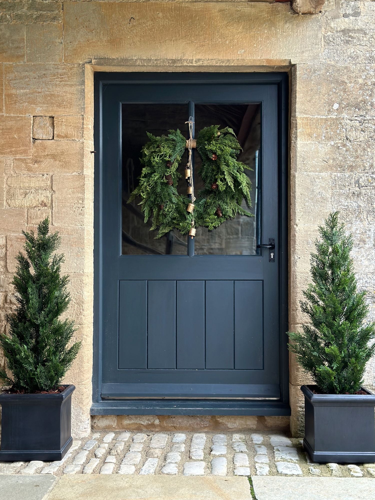 artificial foliage christmas wreath with brass cowbells hanging on a navy door