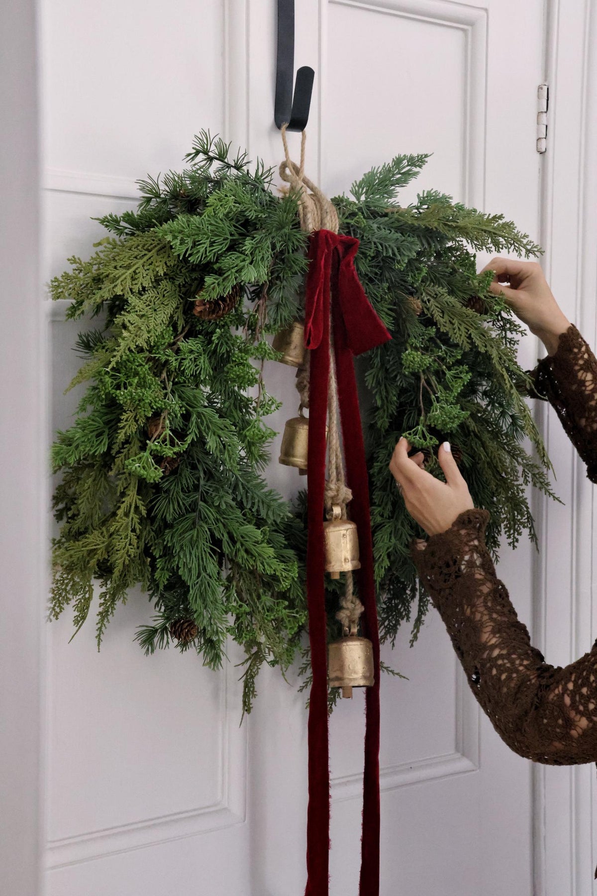large artificial green foliage wreath with brass bells and a long red bow on white door 