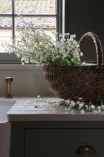 Wicker basket with faux forget me not stems on a kitchen counter near a window.