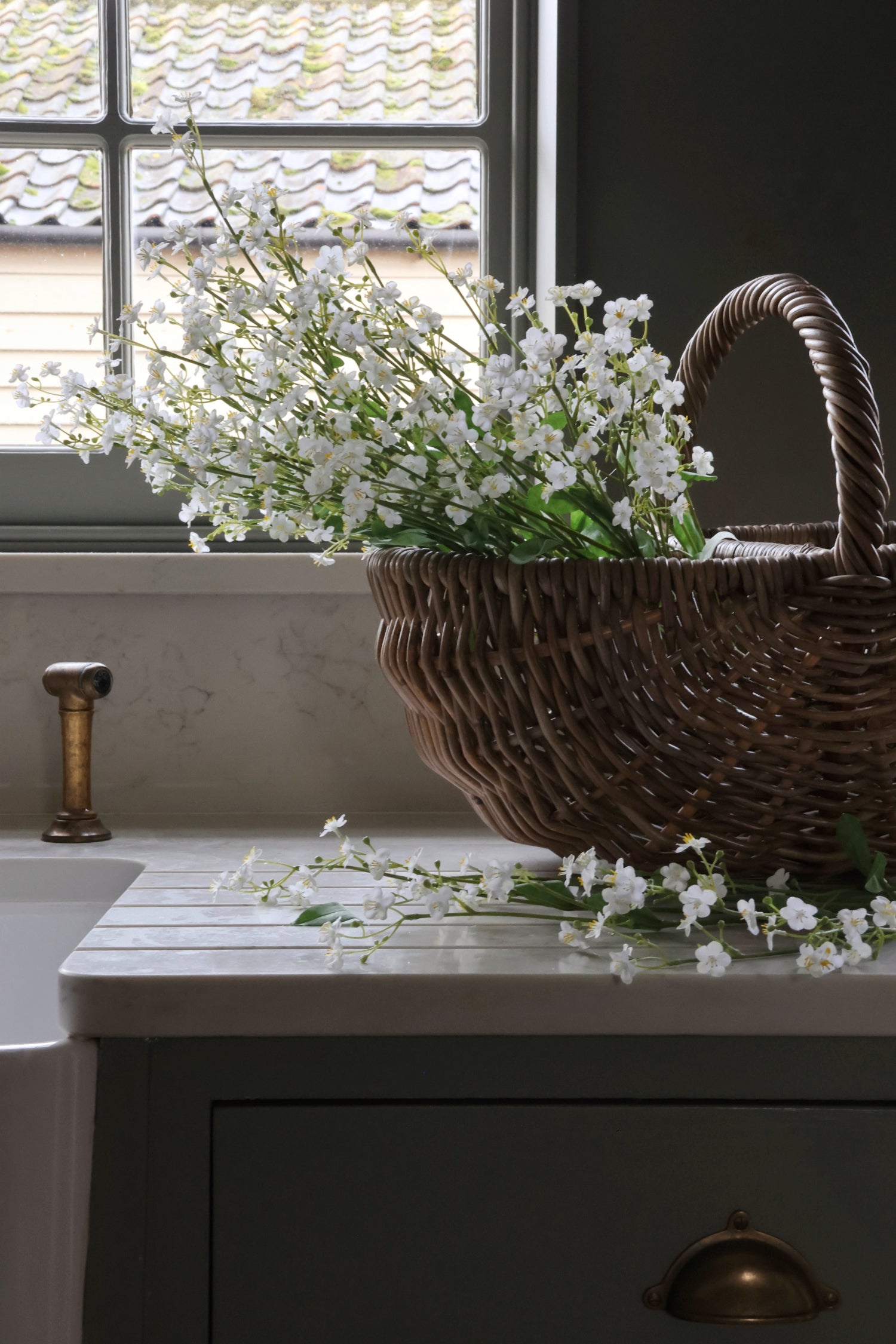 Wicker basket with faux forget me not stems on a kitchen counter near a window.