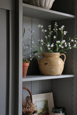 yellow ceramic pitcher with white faux forget me not stems on a dark green shelf