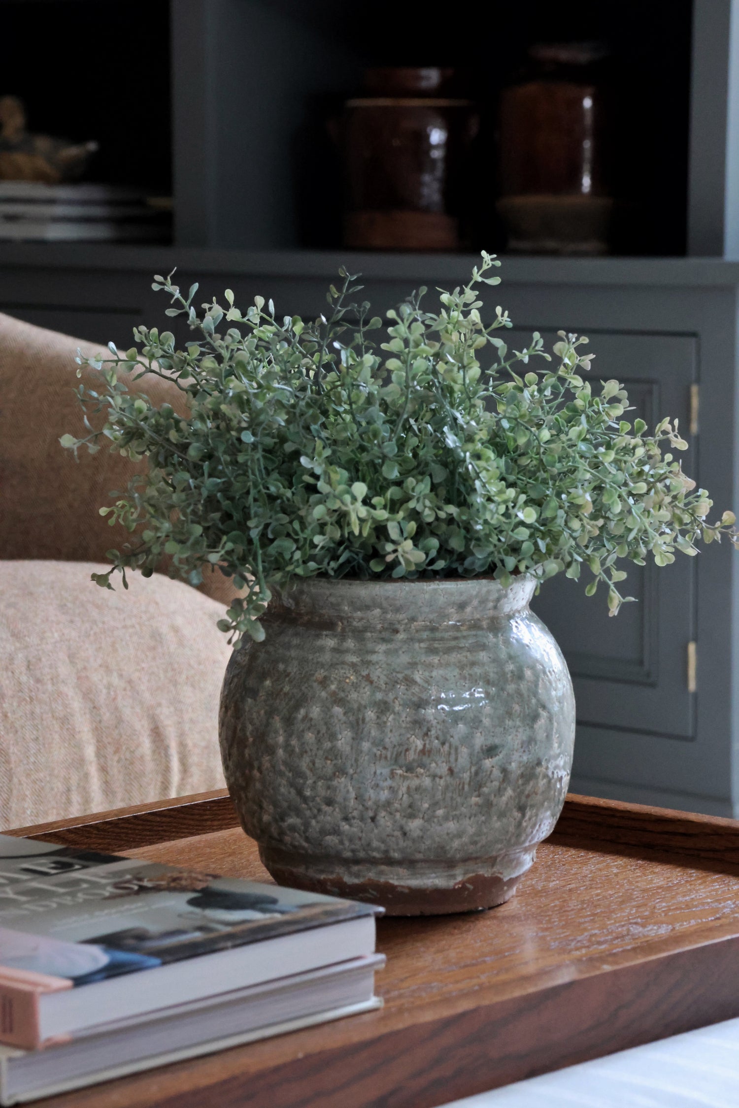 Faux green eucalyptus bush in the Henley pot on a wooden table with books in a home setting